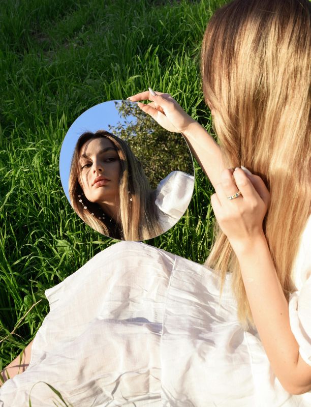 mujer sentada sobre el pasto viendo su reflejo en un espejo